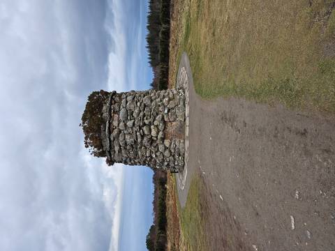       Circular stone memorial cairn standing alone on open moorland
  