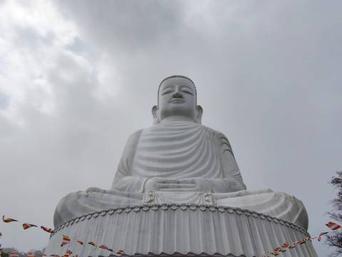       Large white seated Buddha statue rises against a cloudy sky.
  