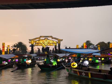       Lantern-lit boats gather on Hoi An’s river as the ornate bridge glows at dusk.
  