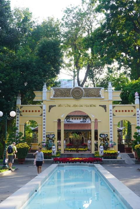       Decorative yellow gateway in a leafy park with a handful of sightseers.
  