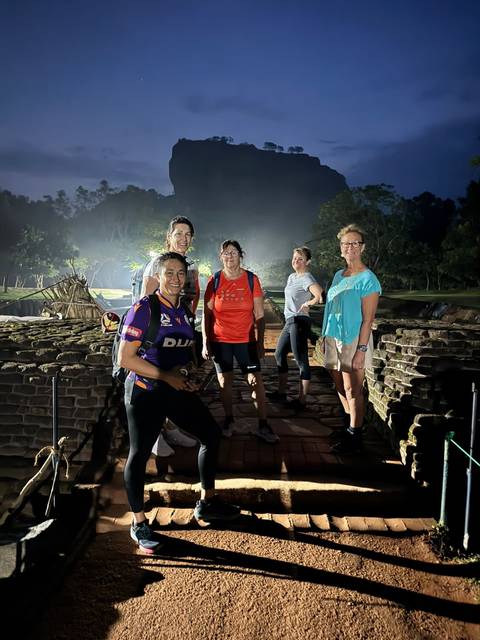       Group of women pose on ancient ruins at night illuminated by spotlights.
  