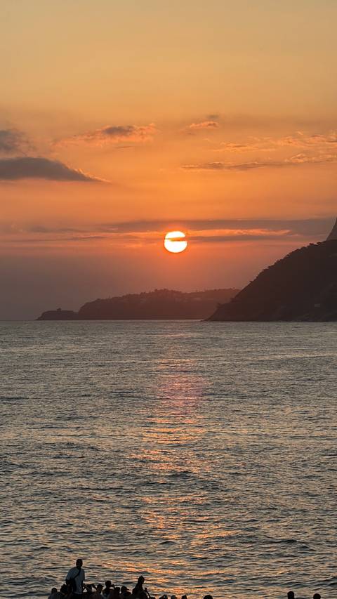       Orange sun setting over the Atlantic Ocean with silhouetted headlands.
  