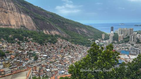       Panoramic view of Rocinha favela with ocean and city towers beyond, text label overlaid at bottom.
  