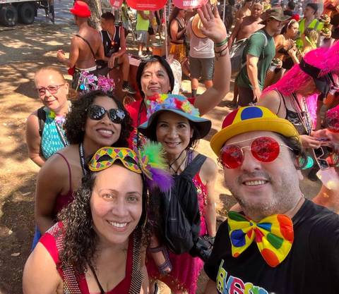       Outdoor carnival selfie with participants wearing vibrant hats, masks, and bow ties.
  
