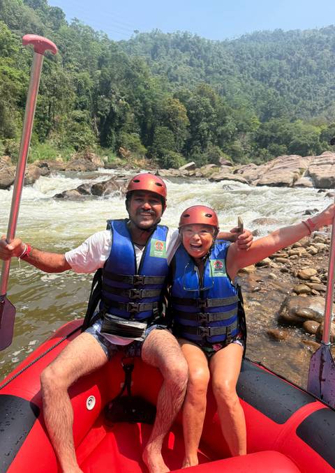       Two adventurers in helmets and life jackets celebrate after white-water rafting on a fast-flowing Sri Lankan river
  