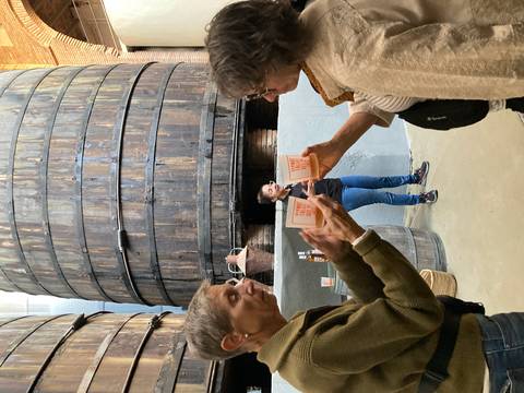       Visitors clink vermouth glasses during a cellar tour in a traditional Spanish bodega with giant wooden barrels
  
