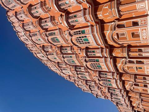       Upward angle of the ornate pink sandstone façade of Hawa Mahal against a vivid blue sky in Jaipur
  