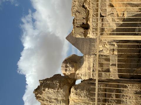       The Great Sphinx with Khafre Pyramid rising behind under a partly cloudy blue sky
  