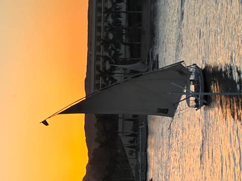       Traditional felucca sailboat glides on the Nile at orange dusk with silhouetted hills
  