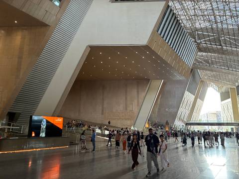       Expansive interior atrium of the Grand Egyptian Museum bustling with visitors under dramatic roof
  