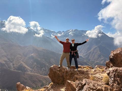       Hikers celebrating atop rocky summit with High Atlas snow-capped peaks behind
  