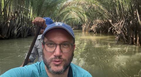       Selfie on a narrow canoe moving through dense palms on a muddy river.
  