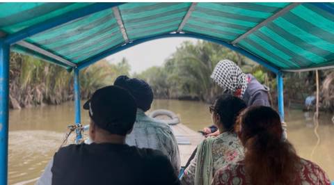       Small group rides under a striped canopy along a muddy jungle canal.
  
