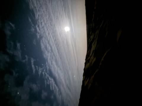       A dim night scene over desert dunes with the moon illuminating thin clouds.
  