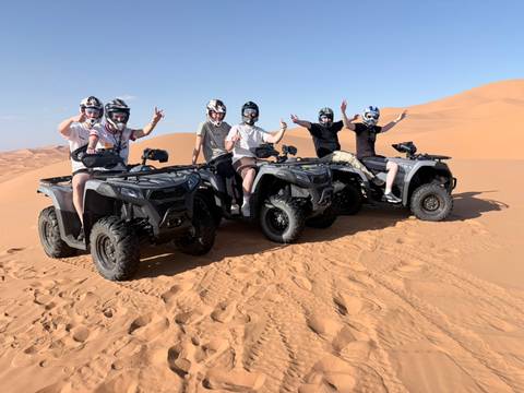       Six riders on quad bikes pose triumphantly on soft desert sand dunes.
  
