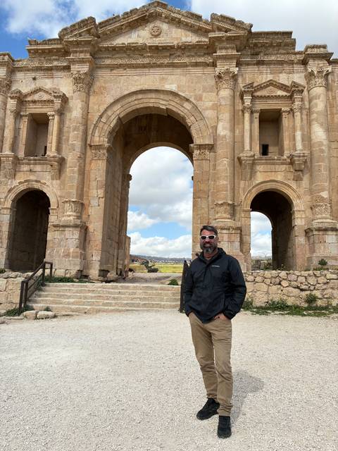       Man standing before the grand Hadrian’s Arch at Jerash archaeological site
  