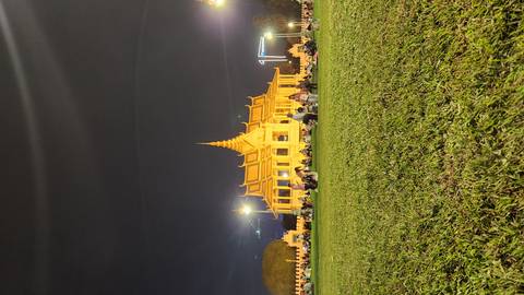       The illuminated Royal Palace pavilion glows at night as crowds relax on the grassy lawn in Phnom Penh.
  