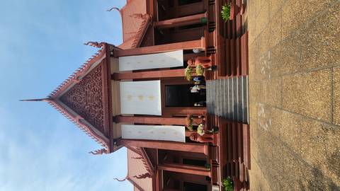       Grand Khmer temple facade with steep red roof, twin lion statues and white decorative banners, seen from the foot of wide stone steps.
  