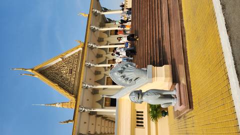       Elegant golden-trimmed temple with intricate gable and naga balustrades as visitors ascend the broad terracotta steps.
  