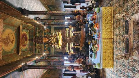       Lavish temple interior featuring a towering gilded Buddha shrine surrounded by smaller statues, offerings and colorful murals.
  