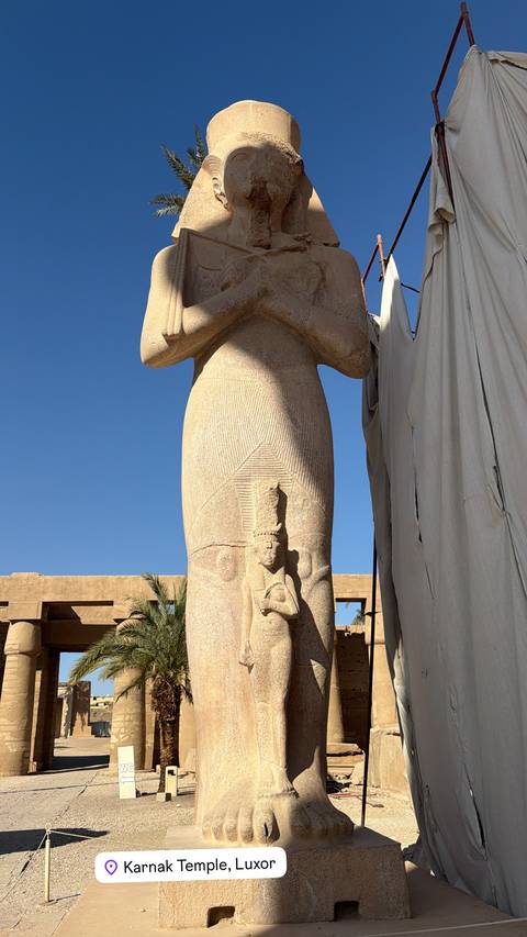       Close-up of a tall ancient Egyptian statue against a clear blue sky.
  