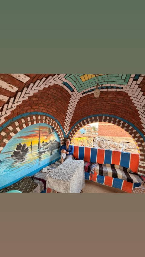       Traveler relaxing inside a brightly painted Nubian house with artistic murals.
  