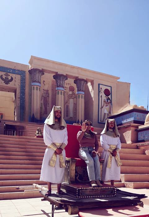       Travellers dressed as ancient guards pose before pharaonic columns and hieroglyphic wall art at a desert film set.
  
