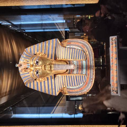       The gold and lapis funerary mask of Tutankhamun displayed under museum lighting.
  