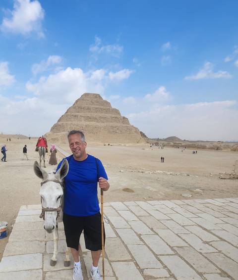       Traveller with a donkey poses in front of the Step Pyramid of Djoser in the Saqqara desert.
  