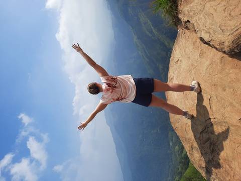       Traveler stands triumphantly on a rocky cliff overlooking lush mountains in Ella, Sri Lanka
  