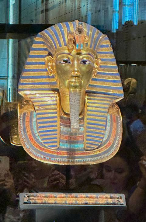       Close-up of the golden funerary mask of Tutankhamun displayed behind glass
  
