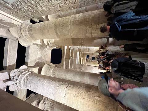       Nighttime scene inside an ancient Egyptian temple with towering hieroglyph-covered columns illuminated for visitors.
  