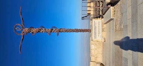       Serpentine bronze cross sculpture atop Mount Nebo against a deep blue sky with panoramic views below.
  