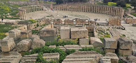       Panoramic view of Jerash’s oval forum ringed by standing columns with scattered visitors exploring the ancient site.
  