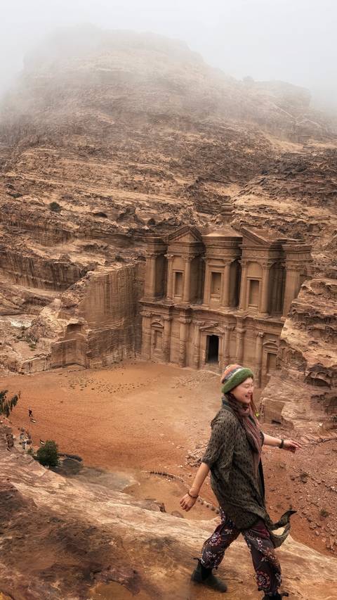       Impressive view of Petra’s Monastery carved into rose-red cliffs as a lone traveler gazes from the overlook.
  