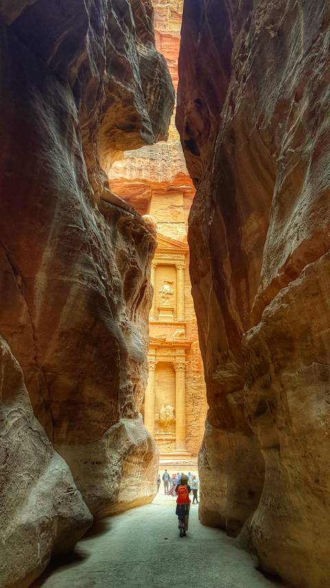       Iconic glimpse of Petra’s Treasury illuminated in warm light, framed by the dark, narrow walls of the Siq.
  