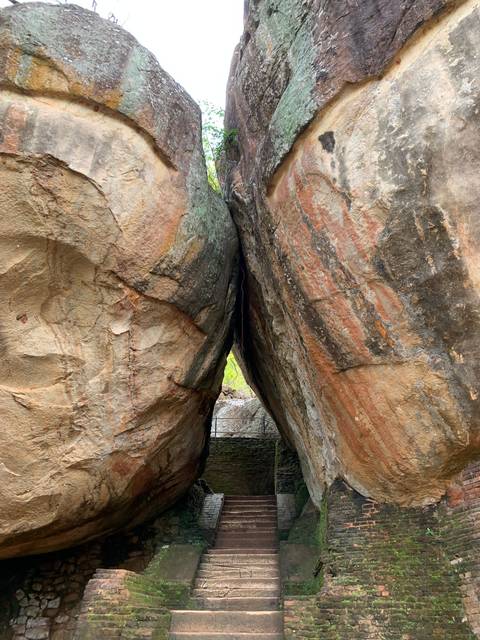       Narrow rock crevice splitting two massive weathered boulders with a glimpse of greenery beyond.
  