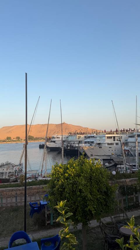       Line of Nile cruise ships moored beside desert hills under pale evening light
  