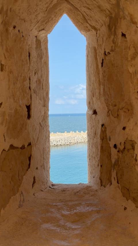      Blue sea framed through a narrow stone embrasure of an old seaside fort
  