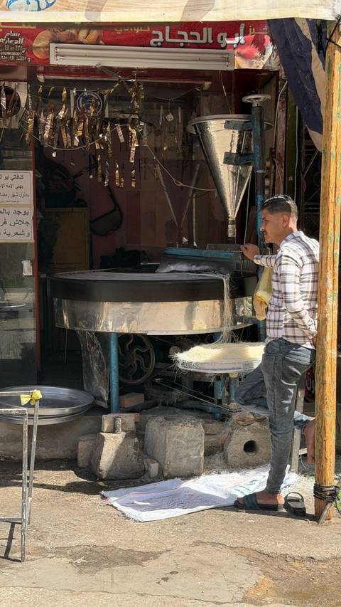       Street vendor stretches fine noodles on a large spinning drum in a Cairo market stall
  