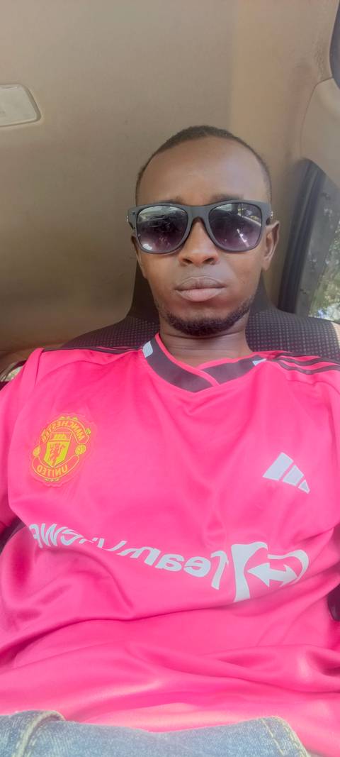       Close-up of a person wearing a pink Manchester United jersey sitting inside a vehicle.
  