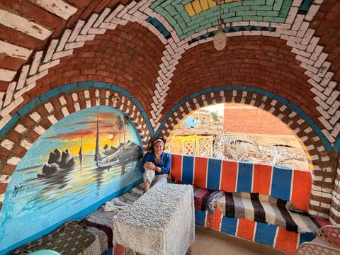       Traveller relaxing under colorful brick arches painted with a Nile sailing scene in a Nubian village
  