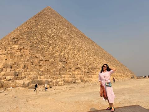       Woman standing beneath the towering limestone blocks of the Great Pyramid under a pale sky
  