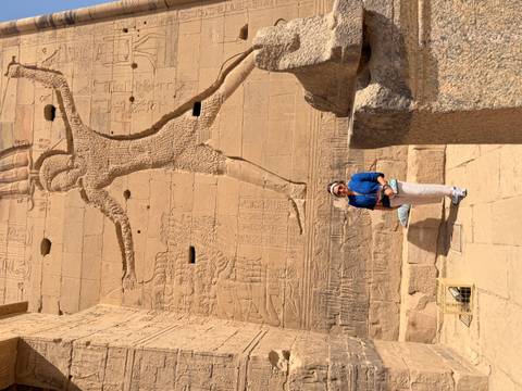       Visitor posing in front of colossal pharaonic relief carvings on sandstone temple walls
  