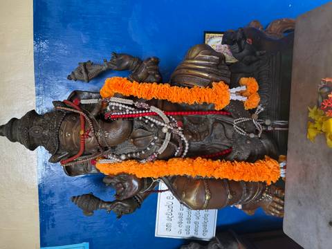       Ornate Ganesha statue adorned with bright garlands against a blue wall.
  