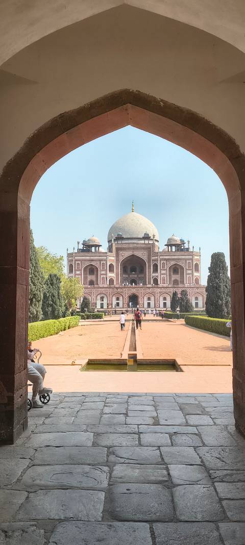      Symmetrical view of Humayun's Tomb framed by arched gateway with manicured gardens and visitors in foreground.
  