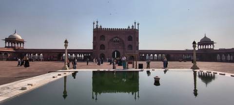       Courtyard of Jama Masjid with reflecting pool and visitors under a clear sky.
  