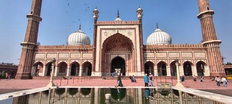       Frontal view of Jama Masjid with twin minarets and domes against a deep blue sky.
  