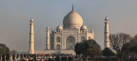       Classic symmetrical sunrise view of the Taj Mahal with soft light and crowds at its base.
  