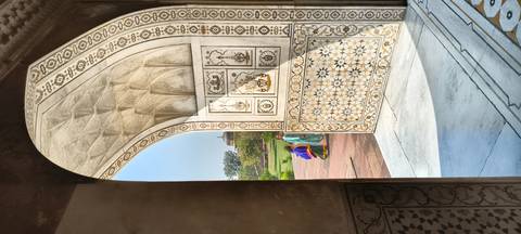       Marble inlaid doorway of a Mughal tomb framing two women in colorful saris outside.
  